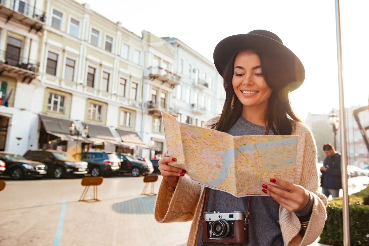 Mulher turista sorrindo olhando mapa em rua europeia com câmera no pescoço