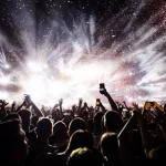 Multidão em show levantando as mãos com luzes e fogos em palco de festival