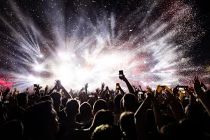 Multidão em show levantando as mãos com luzes e fogos em palco de festival