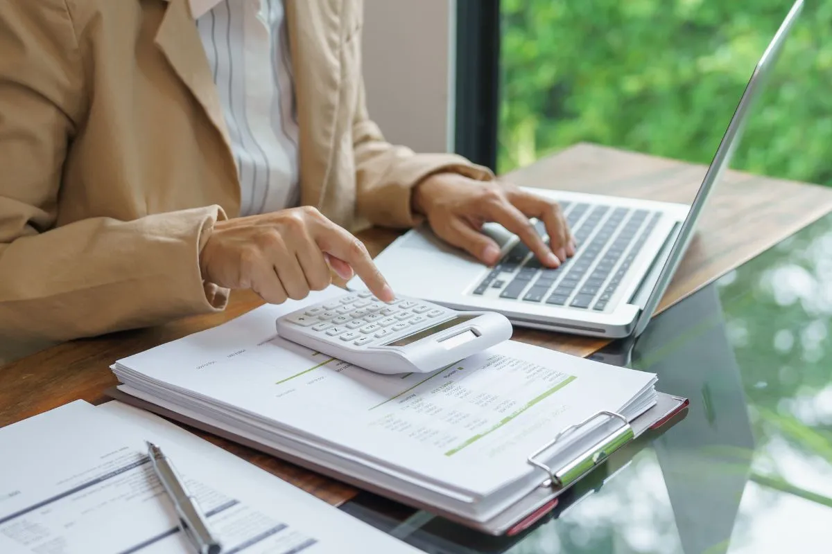Pessoa utilizando calculadora e notebook sobre documentos financeiros para acompanhar indicadores econômicos com clareza.