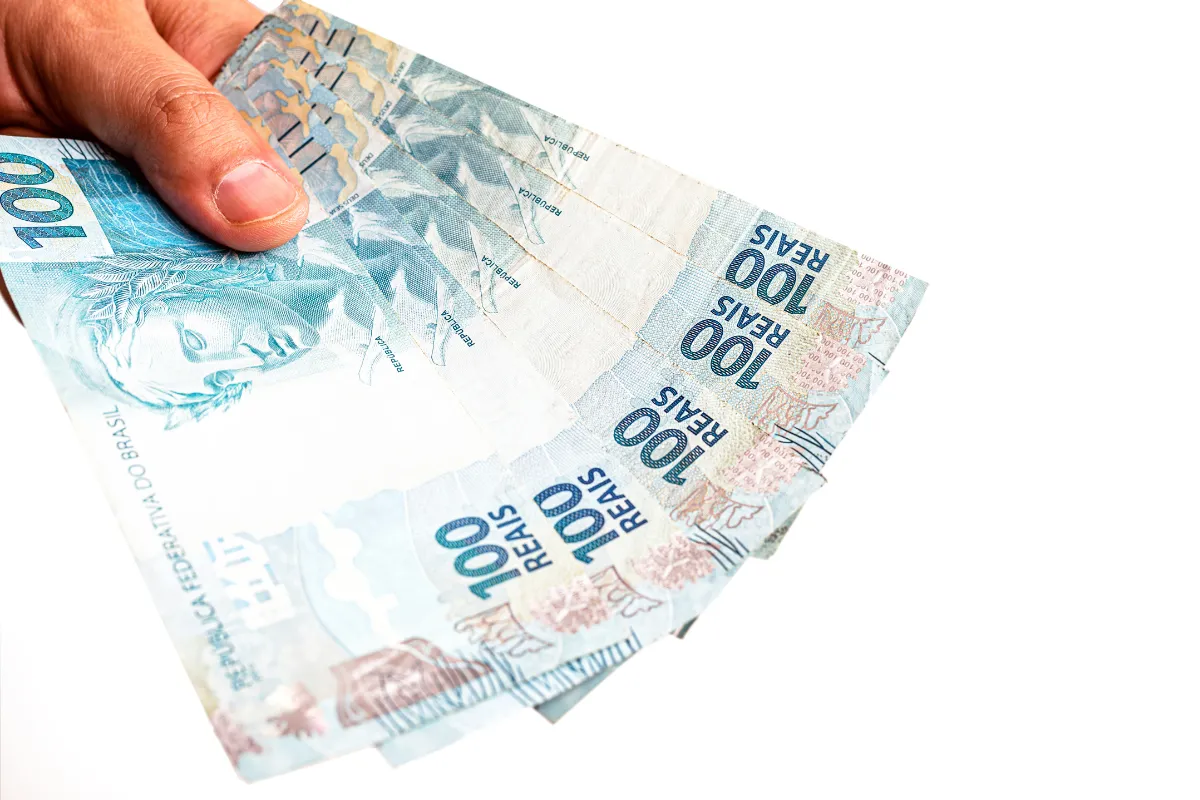 Mão segurando notas de cem reais simbolizando benefícios tributários e incentivos fiscais no Brasil