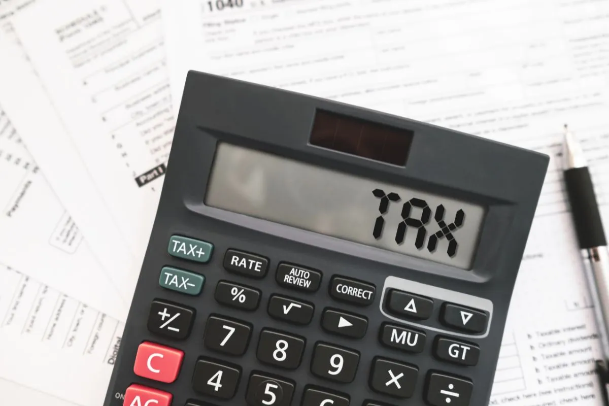 Calculadora com palavra tax no visor sobre formulários financeiros ligados à política fiscal e impostos.