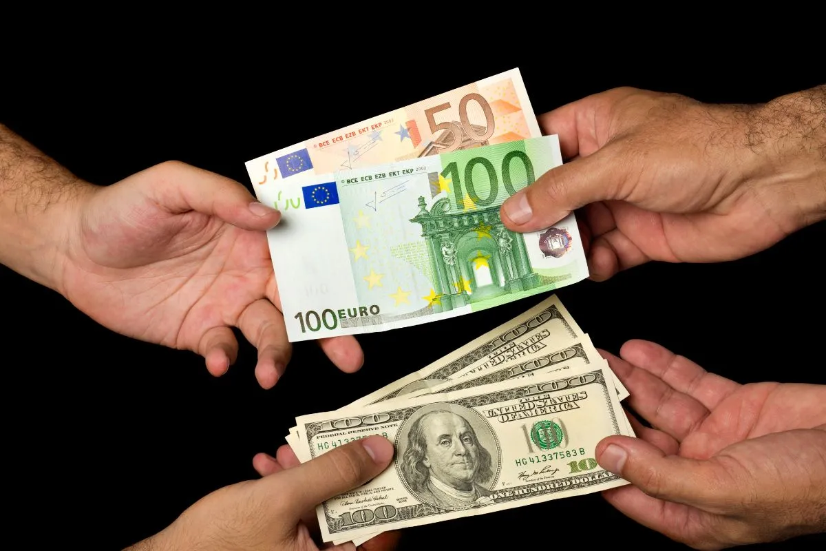 Mãos trocando notas de euro por dólares americanos em operação de câmbio