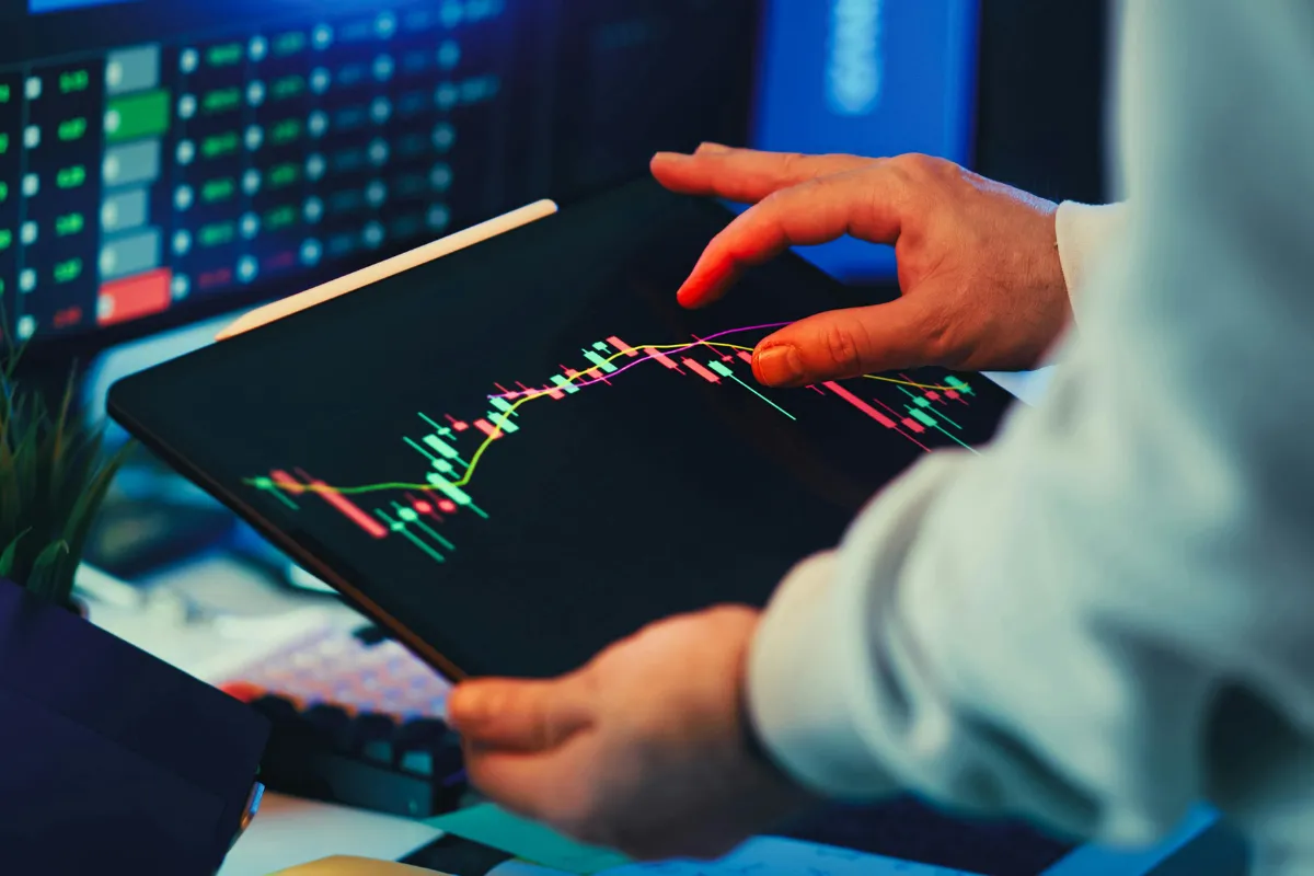 Pessoa analisando gráficos financeiros em tablet relacionado a capital e investimentos no mercado de trabalho