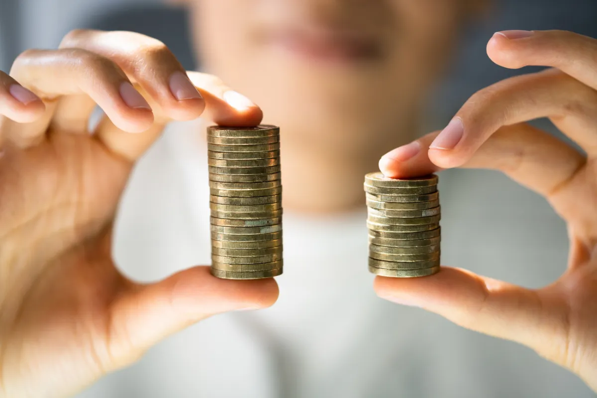 Pessoa comparando duas pilhas de moedas representando diferença de renda e efeitos do salário mínimo 2026