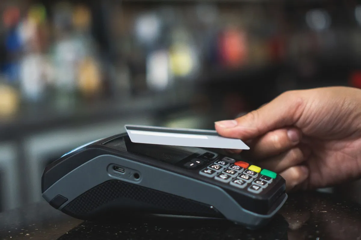 Pessoa passando cartão em máquina de pagamento para realizar compra