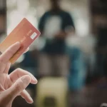 Pessoa segurando cartão de crédito em ambiente comercial desfocado ao fundo