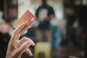 Pessoa segurando cartão de crédito em ambiente comercial desfocado ao fundo