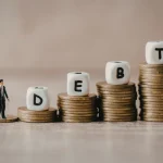 Moedas empilhadas formando a palavra debt representando dívida pública e endividamento econômico do Brasil