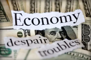Imagem representando crise econômica com notas de dólar ao fundo e palavras recortadas como “economy”, “despair” e “troubles”