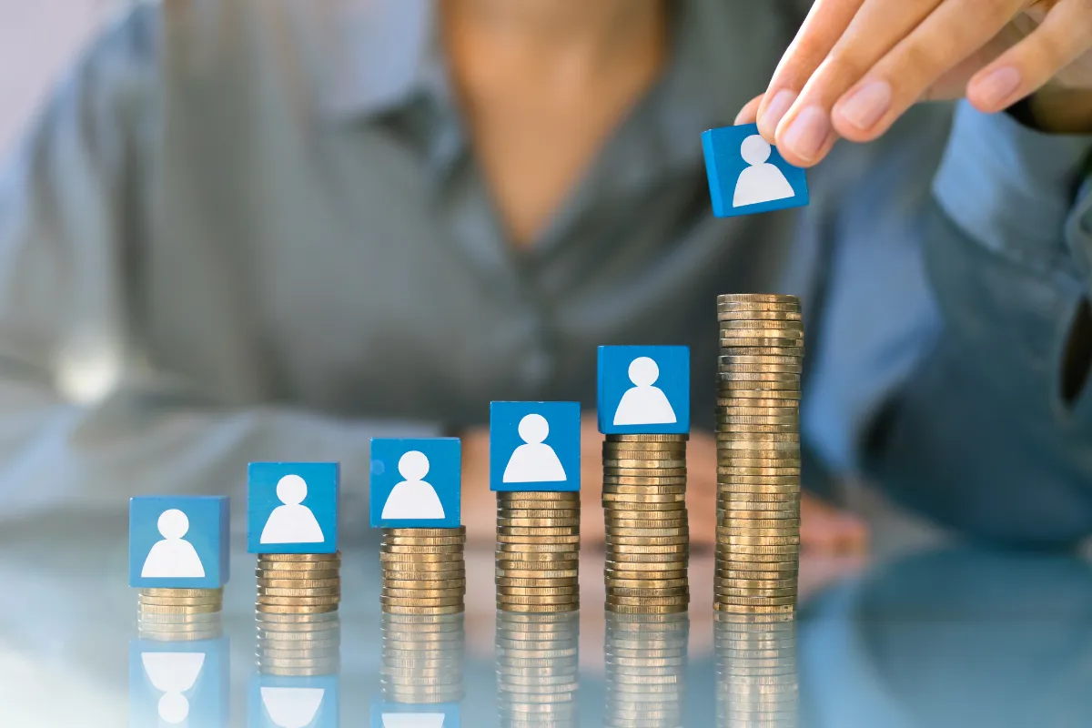 Blocos com ícones de trabalhadores sobre pilhas de moedas simbolizando impacto do salário mínimo na renda