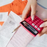 Pessoa usando calculadora sobre recibos e contas representando impacto dos impostos no preço final