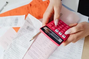 Pessoa usando calculadora sobre recibos e contas representando impacto dos impostos no preço final