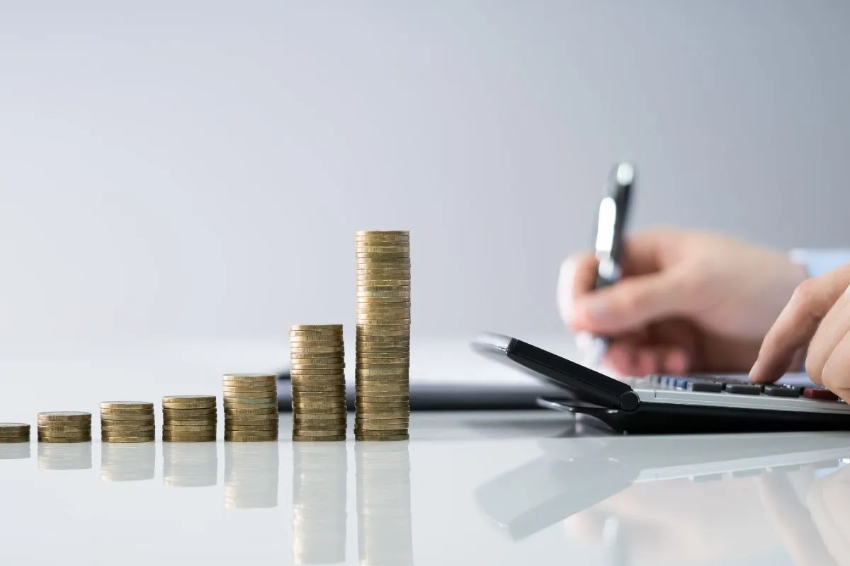 Pilha de moedas em crescimento ao lado de pessoa usando calculadora para planejamento financeiro