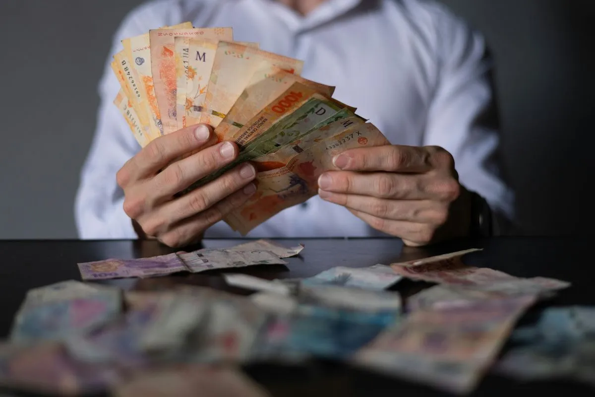 Pessoa segurando e contando notas de real brasileiro sobre mesa com dinheiro espalhado
