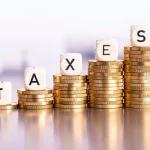 Pilha crescente de moedas com letras formando a palavra taxes representando aumento de impostos