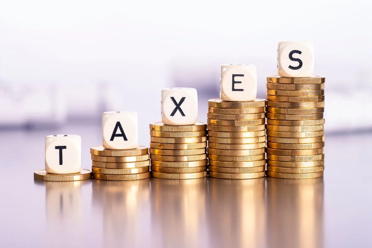 Pilha crescente de moedas com letras formando a palavra taxes representando aumento de impostos