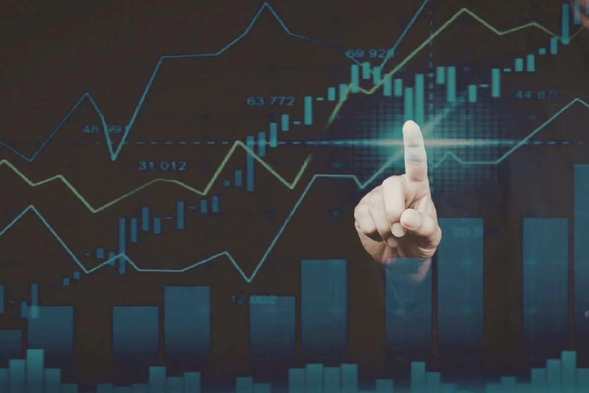 Pessoa apontando para gráfico financeiro digital com dados econômicos usados para análise de mercado e investimentos.