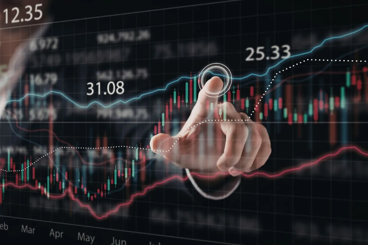 Tela com gráficos de mercado e mão interagindo com dados financeiros para acompanhar indicadores econômicos em tempo real.