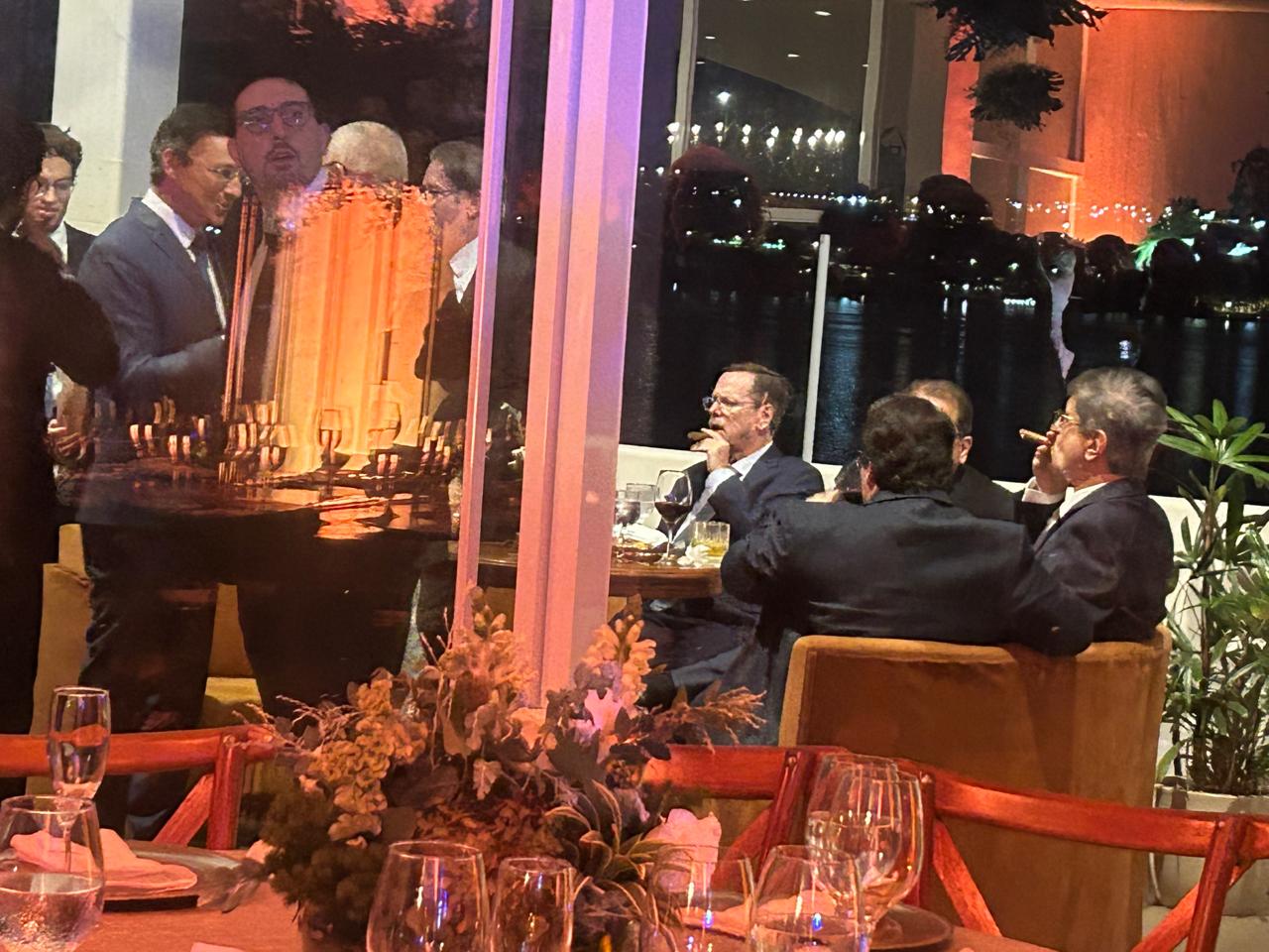O procurador-geral da República, Paulo Gonet, aparece sentado no sofá, entre dois homens, fumando charuto - 12/5/2026 | Foto: Cristyan Costa/Revista Oeste