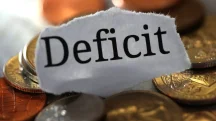 Palavra deficit sobre moedas representando rombo fiscal e desequilíbrio nas contas públicas brasileiras