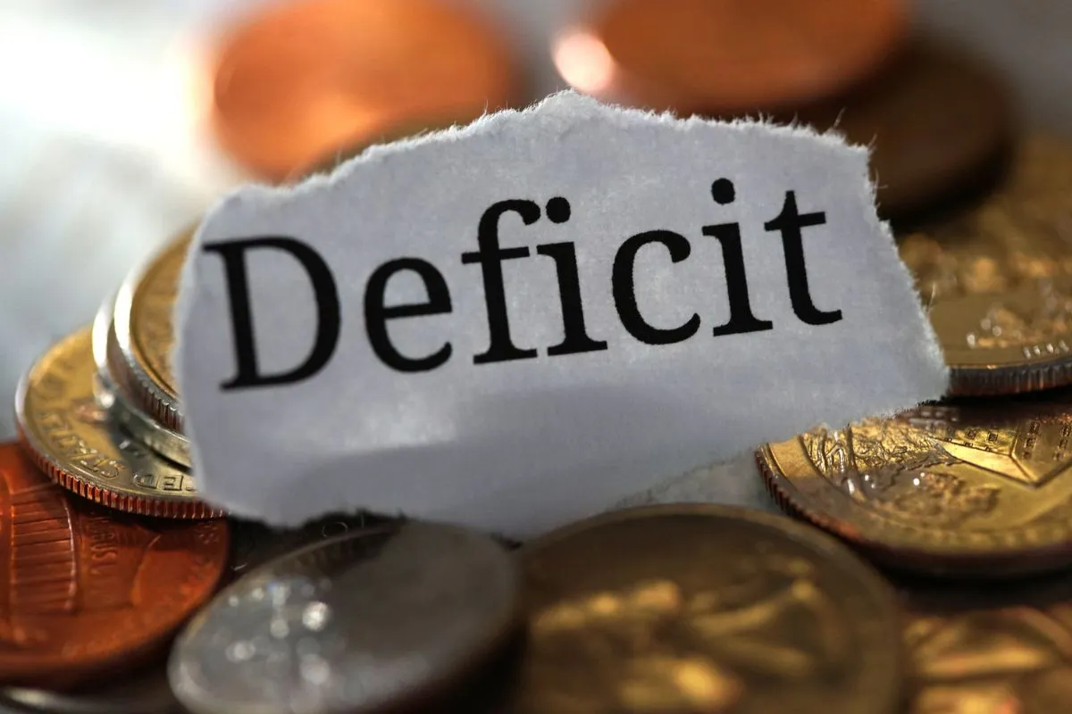 Palavra deficit sobre moedas representando rombo fiscal e desequilíbrio nas contas públicas brasileiras