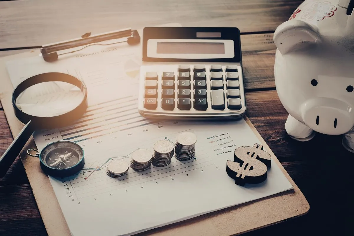 Mesa com calculadora, moedas e cofre ilustrando planejamento financeiro e análise econômica pessoal em ambiente doméstico.