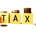 Blocos com a palavra tax e moedas empilhadas representando os principais impostos e a carga tributária brasileira