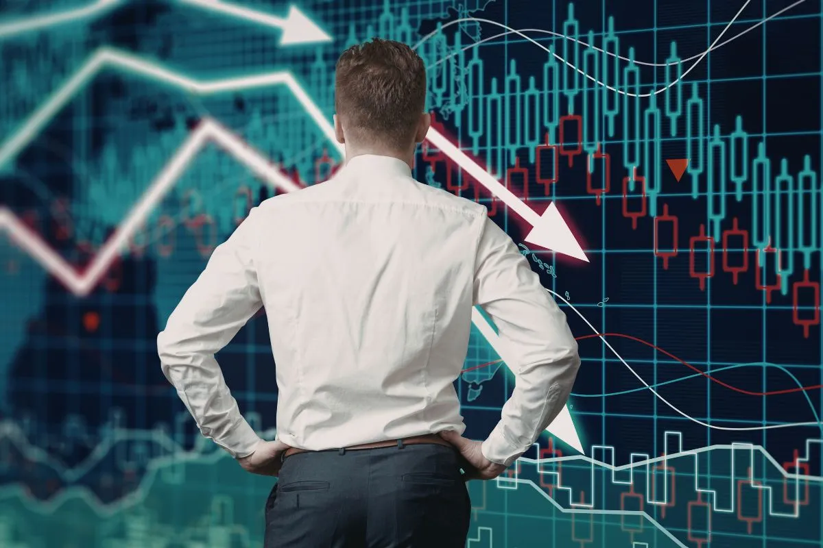 Homem observando gráficos de queda no mercado financeiro ligados a riscos econômicos e proteção patrimonial.