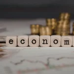 Cubos formando a palavra economy sobre gráficos financeiros, representando reforma econômica e modernização do mercado