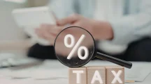 Lupa destacando símbolo de porcentagem sobre blocos com palavra tax em cenário de análise tributária.
