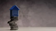 Miniatura de prédio sobre pilha de moedas simbolizando teto de gastos e limite das despesas públicas.