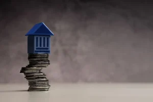 Miniatura de prédio sobre pilha de moedas simbolizando teto de gastos e limite das despesas públicas.