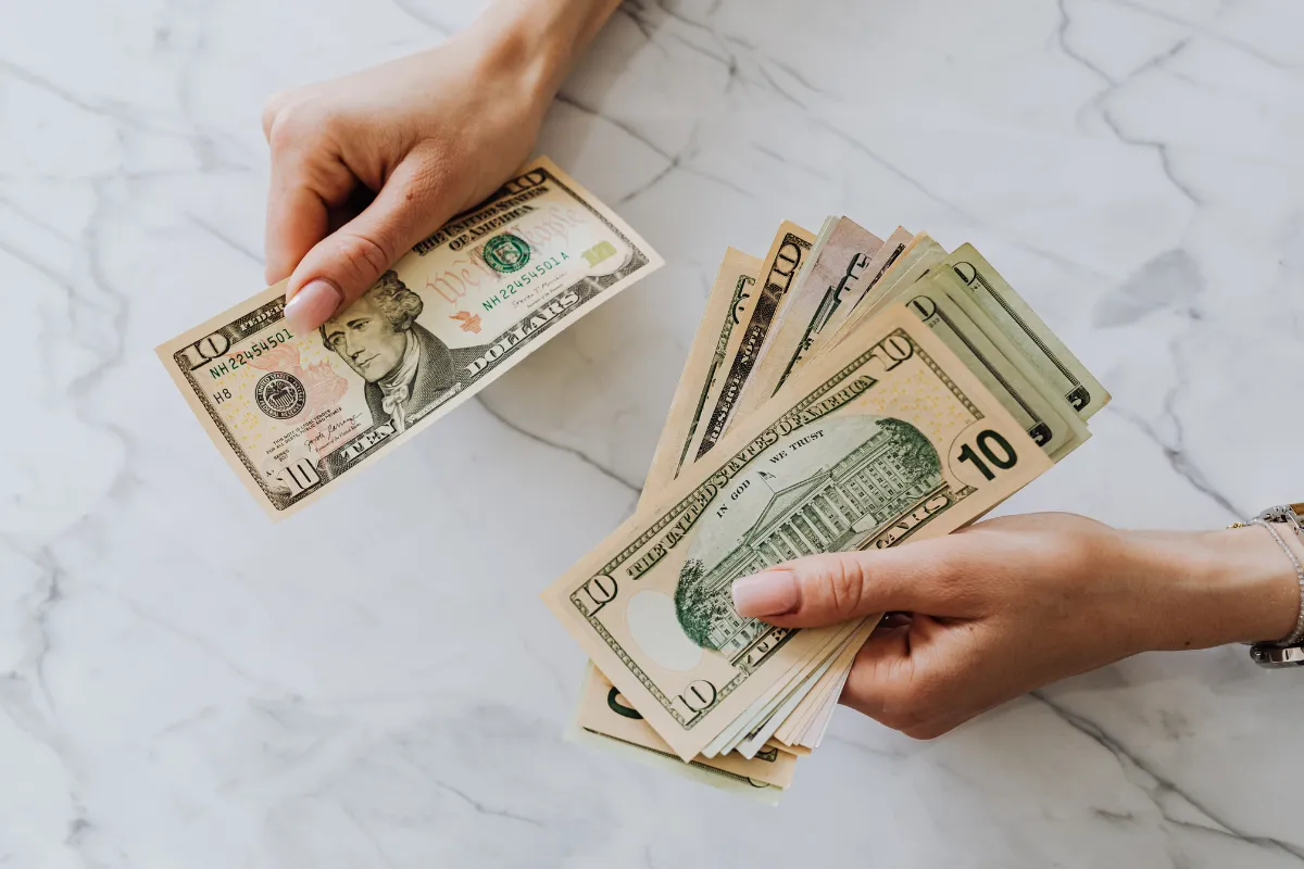 Mãos segurando notas de dólar sobre mesa clara representando transferência de recursos e política fiscal