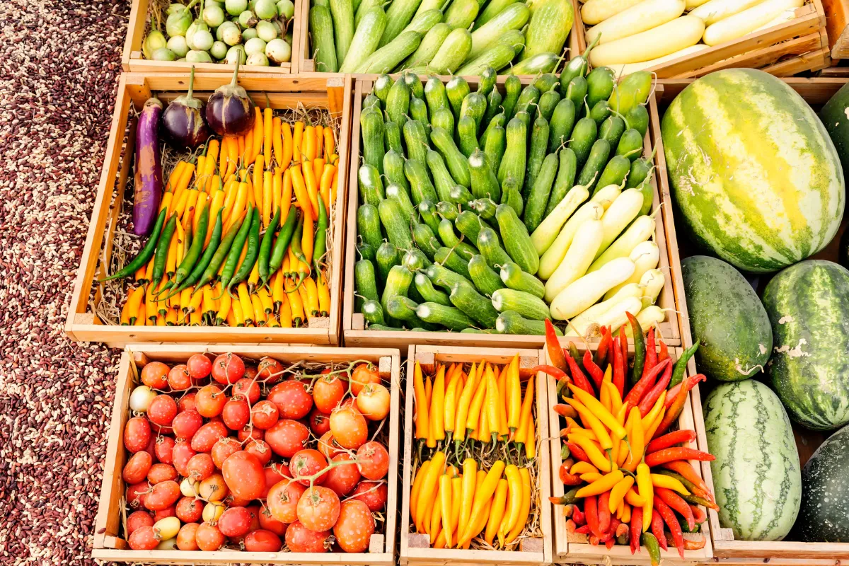 Caixas com frutas, legumes e verduras organizadas em feira mostrando a relação entre agronegócio e preço dos alimentos.