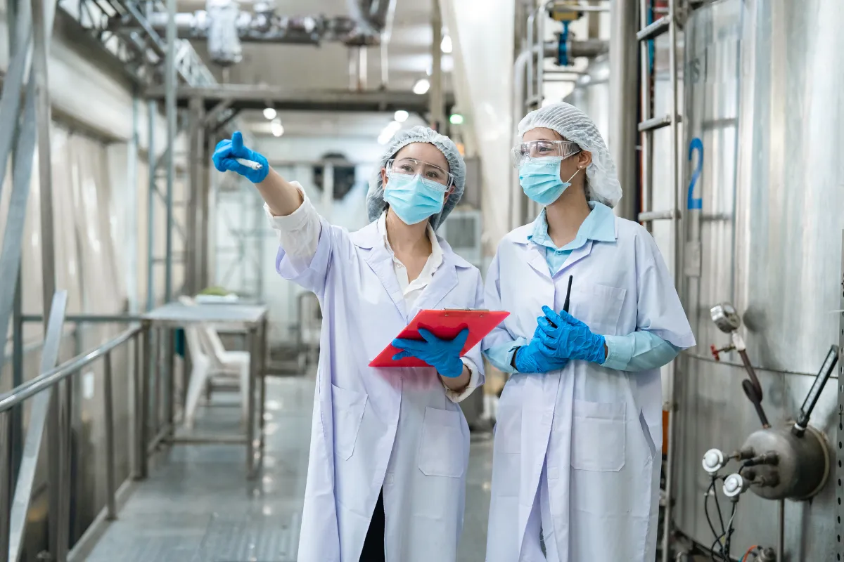Técnicas inspecionam instalações industriais com equipamentos de proteção para atender exigências sanitárias internacionais.