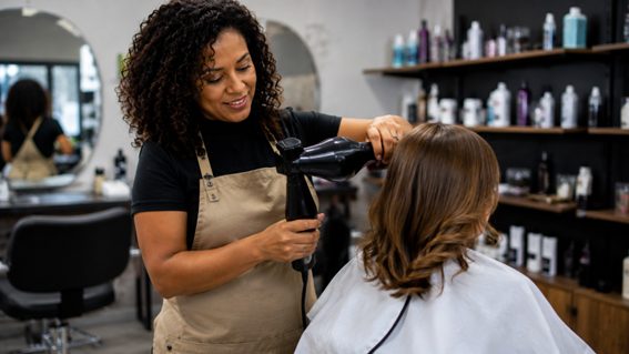 Cabeleireira sorrindo enquanto usa um secador de cabelo profissional em uma cliente dentro do sal�o de beleza.
