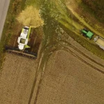 Vista aérea de colheitadeira e trator transportando grãos durante a colheita em uma área agrícola.