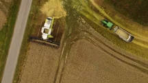 Vista aérea de colheitadeira e trator transportando grãos durante a colheita em uma área agrícola.