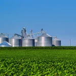 Silos de armazenamento ao lado de lavoura mostrando etapa logística da agroindústria no agronegócio.