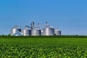 Silos de armazenamento ao lado de lavoura mostrando etapa logística da agroindústria no agronegócio.