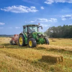Trator agrícola trabalhando em lavoura durante período de colheita e enfardamento.