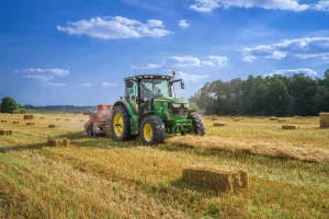 Trator agrícola trabalhando em lavoura durante período de colheita e enfardamento.