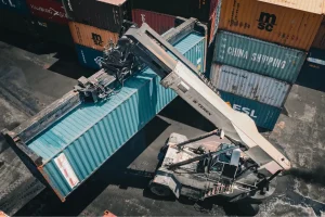 Guindaste movimentando contêiner de carga em pátio logístico destinado ao comércio exterior.