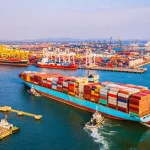 Navio de carga carregado com contêineres navegando em terminal portuário de grande movimentação.