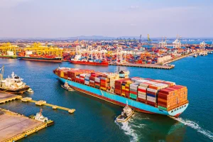 Navio de carga carregado com contêineres navegando em terminal portuário de grande movimentação.