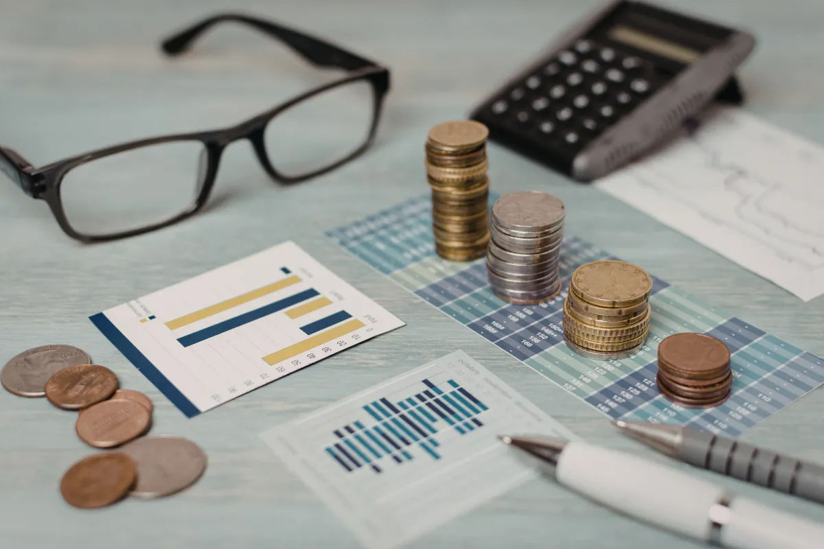 Gráficos, moedas e calculadora sobre mesa representam gestão financeira e análise de investimentos no agronegócio.