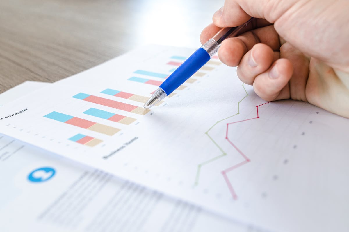 Mão apontando para gráfico de barras e linhas em relatório de análise financeira