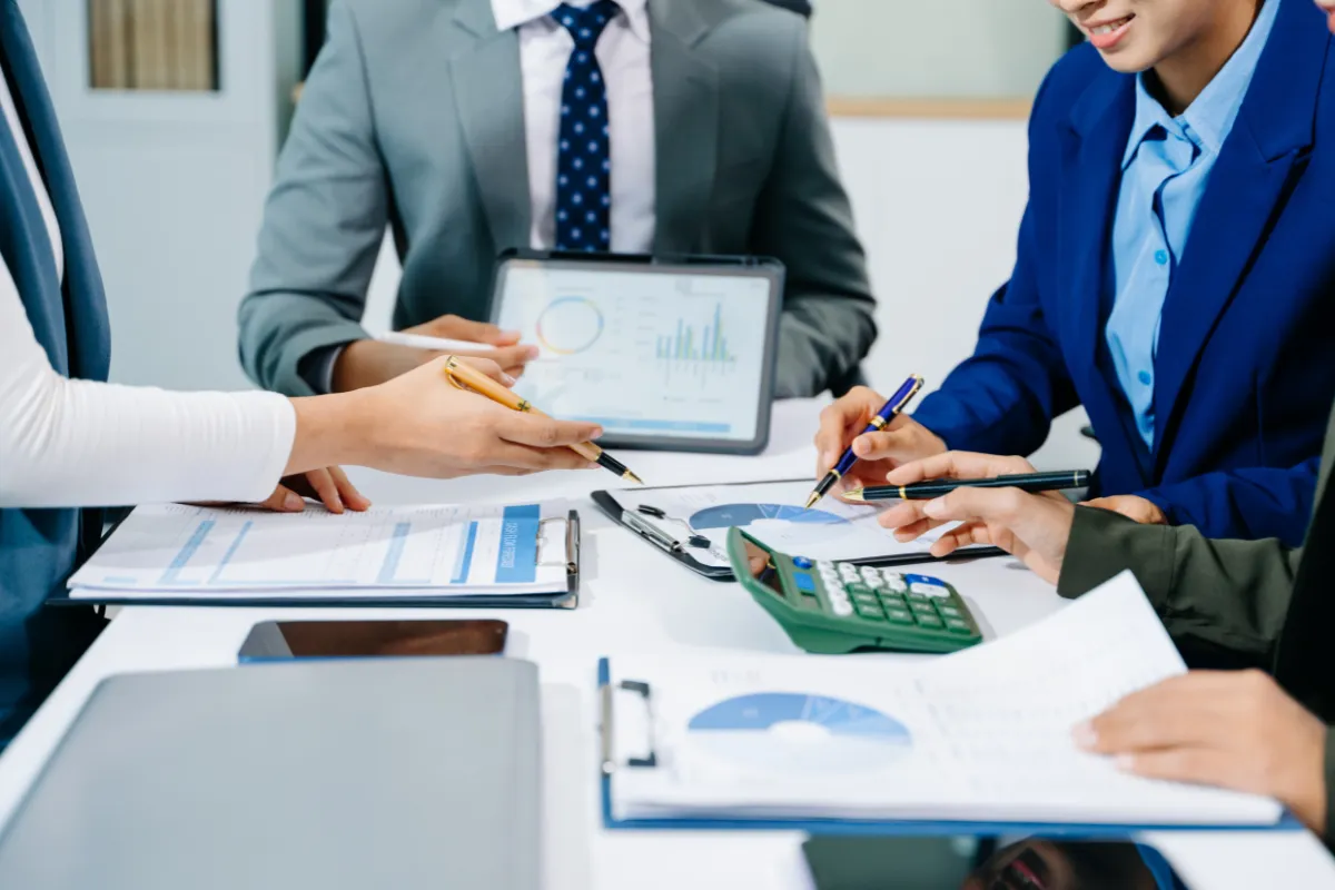 Profissionais reunidos em uma mesa analisando relatórios financeiros e gráficos em ambiente corporativo.