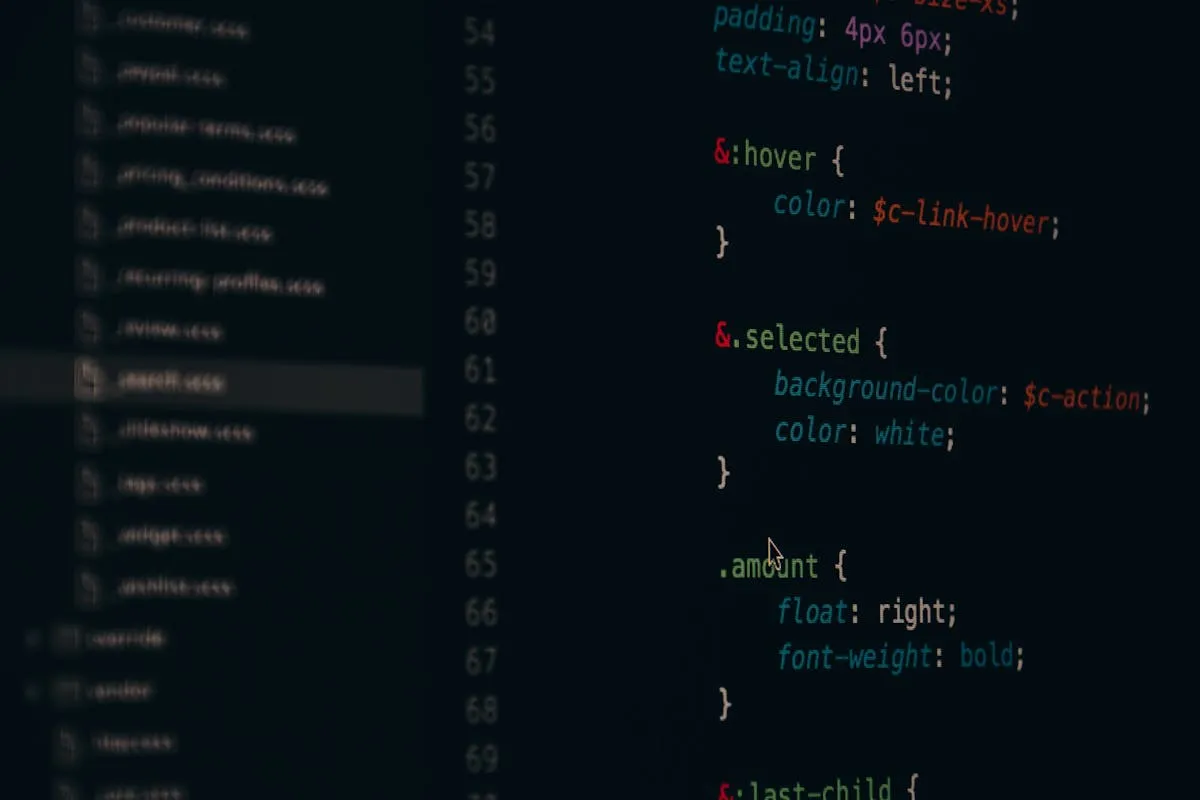 Close-up em ângulo diagonal da tela de um monitor exibindo linhas de código de programação SCSS em fundo escuro, com termos como hover, selected e amount destacados em cores verde, vermelho e azul, ao lado de uma barra lateral com ícones de arquivos.